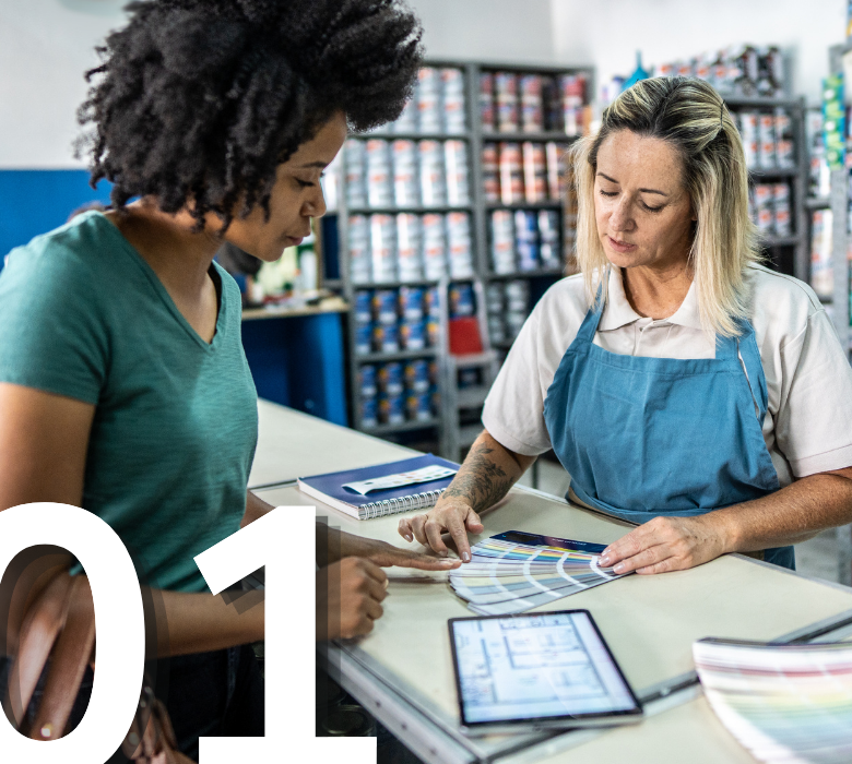 A paint store clerk helping a customer view paint color swatches at the sales counter