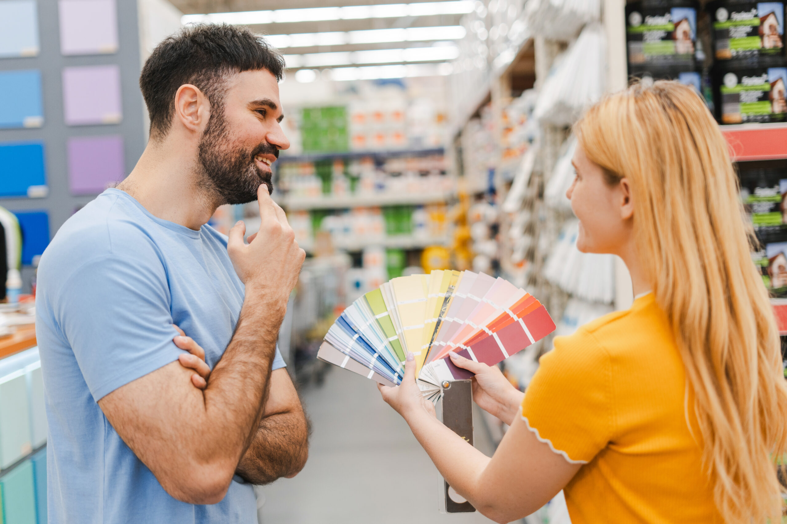 A woman and man viewing a fan deck of paint swatches at a home improvement store