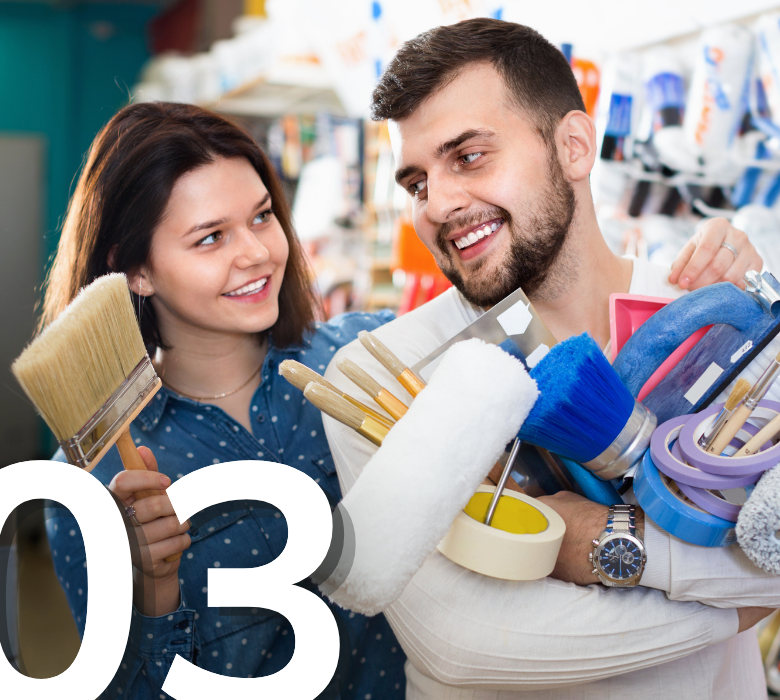 A smiling couple holding arms full of painting supplies for a home renovation project